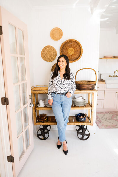 woman wearing black and white blouse with jeans  standing in front of rustic kitchen cart and boho basket decor