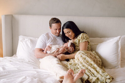 A family cuddles together on their bed with their newborn baby, photographed by a Northern Virginia family photographer during an intimate in-home session.