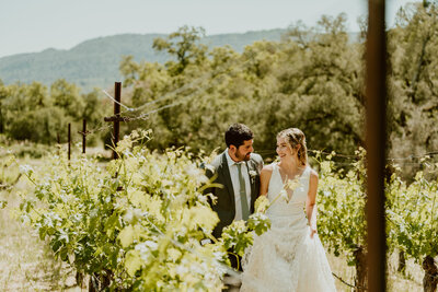 Couple grins at each other as they walk down a vineyard row in Sonoma Valley on their wedding day 