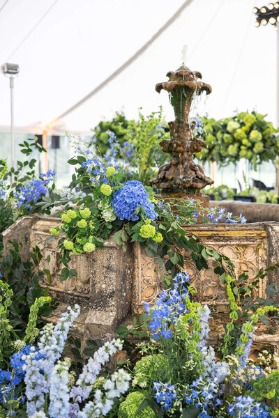 a working fountain decorated in blue and green flowers inside a marquee for a luxury birthday party designed by westacott weddings and events