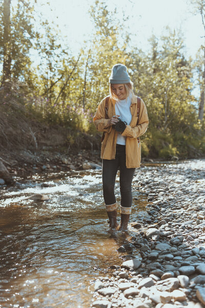 Photographer holding a camera in a forest near water during early fall.
