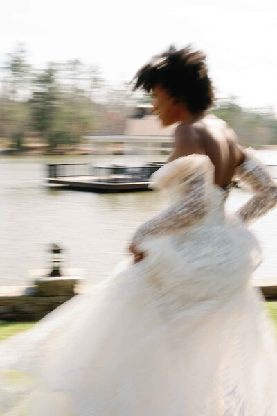 Bride in flowing lace gown walking near a waterfront dock.