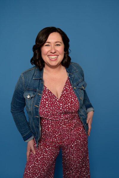 A connecticut wedding photographer smiles and poses for a photo of herself against a blue backdrop