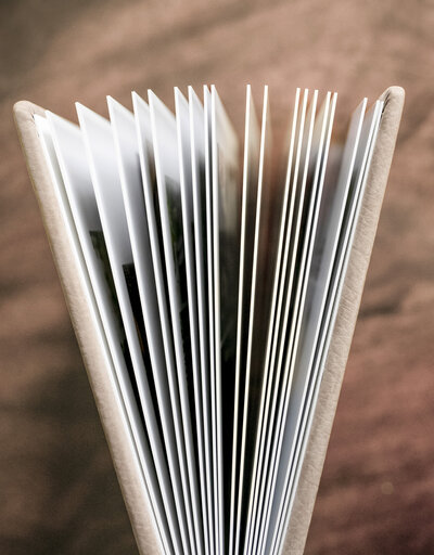 An open photo album viewed from above, revealing several thick pages. The background is a soft, brown fabric surface that contrasts with the crisp white pages of the album.