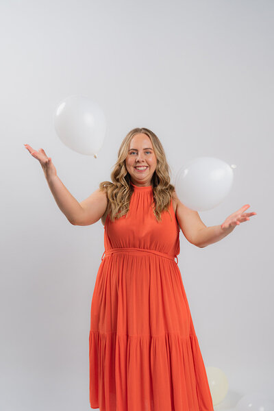 A woman throwing balloons wearing an orange dress