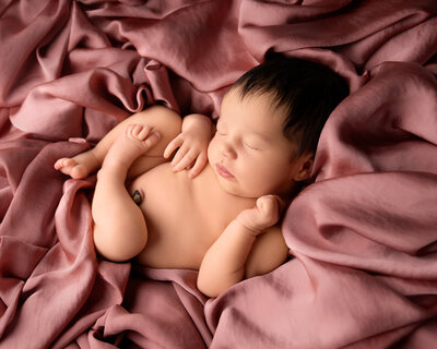 Nyfødt baby sover fredelig på mykt rosa teppe under fotografering i studio nær Oslo.