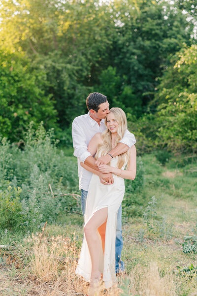 A photo of a couple sharing a moment at a location in Lewiston, Idaho, he has her wrapped in his arms and kissing her temple while she smiles the camera