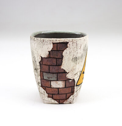 A ceramic cup that resembles plaster falling apart from red bricks with painted cacti and graffiti