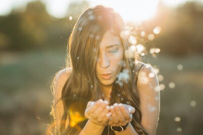 Young woman blowing dandelions from her hands.