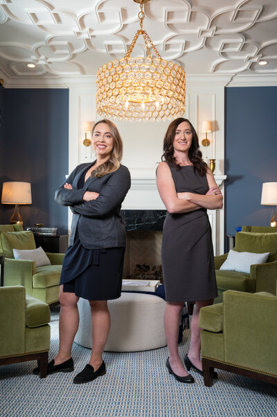 Two poised businesswoman in blazers and heels standing arms folded in luxury sugar house home radiating confidence and sophistication.