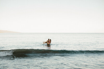 Guy carries his girlfriend out of the ocean water. Photographed by Hawaii Photographer Mersadi Olson