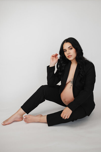 Woman poses while seated in black suit showing her pregnant belly.