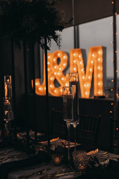 Large illuminated "&amp;m" letters at a wedding in Illinois with tables set up in the foreground, creating a warm and elegant atmosphere.