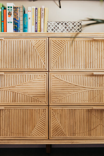 A close up of a pencil reed dresser with books on top of it. 