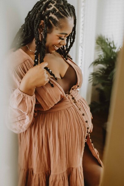 Pregnant woman with locs smiling in a peach dress, soft indoor studio light in Macon, GA.