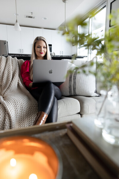 A woman sitting on a couch with a laptop, surrounded by cozy decor and greenery, highlighting a professional branding moment.