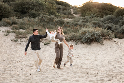 Vrolijk gezin met twee jonge kinderen rent hand in hand door de duinen tijdens een gezinsshoot bij golden hour.