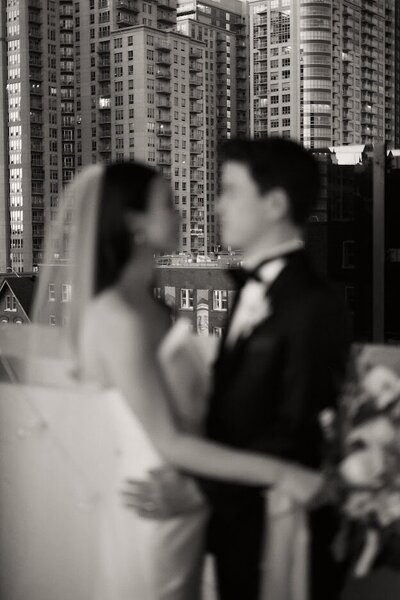Blurry black-and-white photo of a bride and groom standing outside with a crisp downtown cityscape focused in the background.