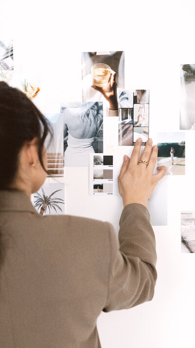 "Brand styling with photos arranged on the wall, featuring a girl meticulously arranging images – Amare Creative.