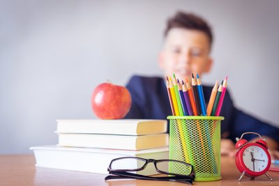 child sitting at table behind colored pencils and a stack of books with an apple on top