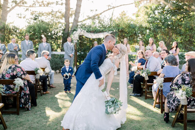 Groom dips and kisses his new Bride as they stop in the aisle between guests