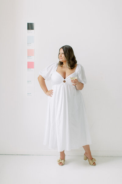 Brunette woman wearing white dress with PANTONE swatches on the wall