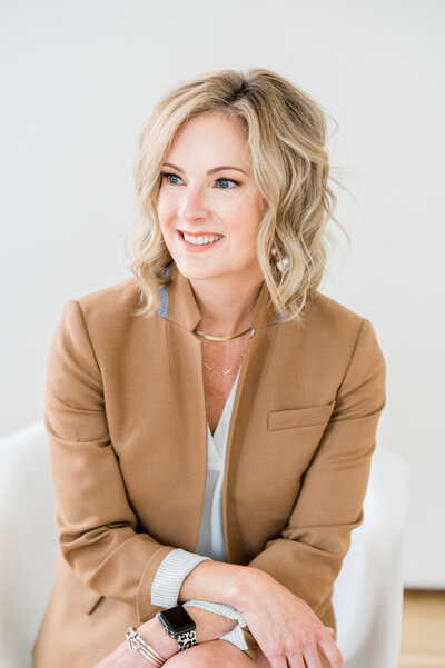 Julie Ladimer in a camel-colored blazer smiling at positive reviews from happy Wills in a Week clients