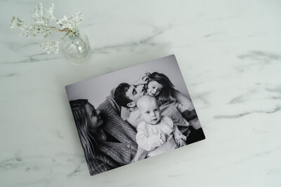 A black and white framed family photo is displayed on a marble surface with a sprig of greenery beside it.