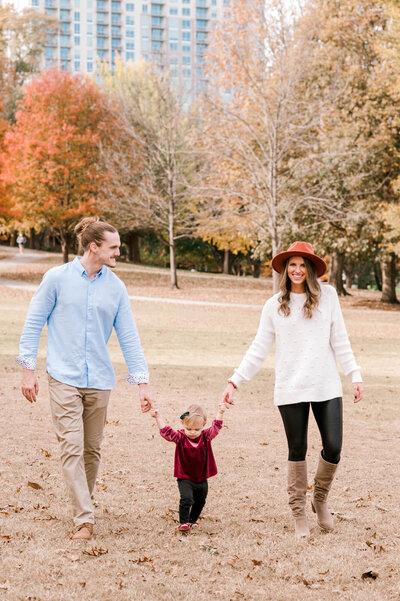 Photographer & husband and 1 year old daughter walking through Piedmont Park in Atlanta Georgia during the fall transition amongst beautiful red, green, orange and yellow trees
