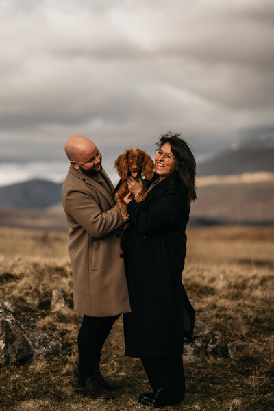 miling wedding photographer and videographer duo holding their happy dog in the Lake District hills. Capturing love stories across the Lake District and destination weddings worldwide.