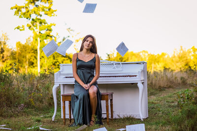 Graduating Senior sitting on piano bench with music sheets in air | Senior Photography