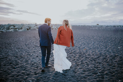 Bride and groom embrace on Iceland’s black sand beach with scattered glacier chunks, a magical scene with an Iceland wedding photographer.