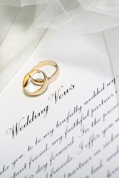 A pair of gold wedding rings sit on top of the written vows for the wedding.