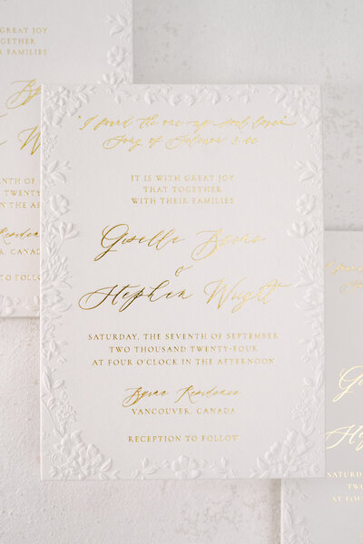 Gold foil calligraphy invitation on white cardstock with floral sculpted emboss