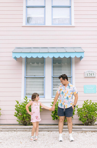 A daughter and her dad posing in front of a pink building