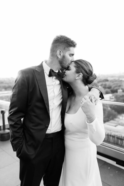 Black and white photo of man kissing bride on forehead