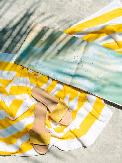 Magazine and yellow sandals laying on yellow striped towel