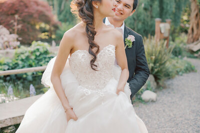 groom carrying brides train and smiling at her from behind