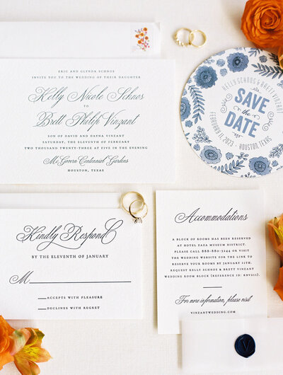 Flat lay of wedding invitation suite with wedding rings and orange flowers