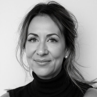 A woman with shoulder-length brown hair, Cristina Horvath, CEO of Sweet Pea Ink Creative, wearing a white button-up shirt and beige pants stands with her hands in her pockets, embodying the modern professionalism of Sweet Pea Ink Creative’s brand design, against a plain white background.