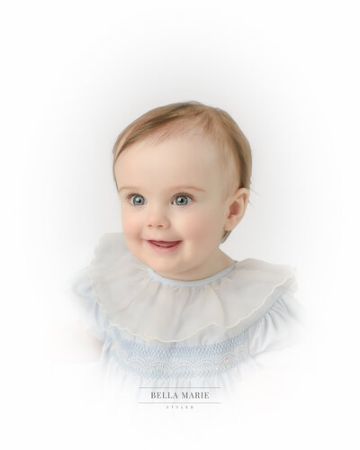 Ten month baby girl with brght blue eyes smiling for her heirloom portrait wearing a vintage blue dress with large white collar