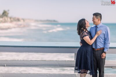 Soon to be married couple cozy up to each other and smile as they pose for engagement photos on the San Clemente Pier