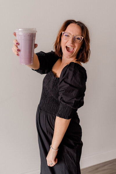 Rachel Hahn, owner, smiles big at the camera with a purple drink in her hand.