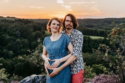 Těhotná maminka držící se za svoje bříško na louce při západu slunce
