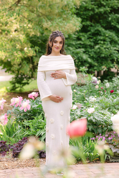 Expecting mom standing in a beautiful, colorful garden, holding her baby bump for her louisville maternity photography session