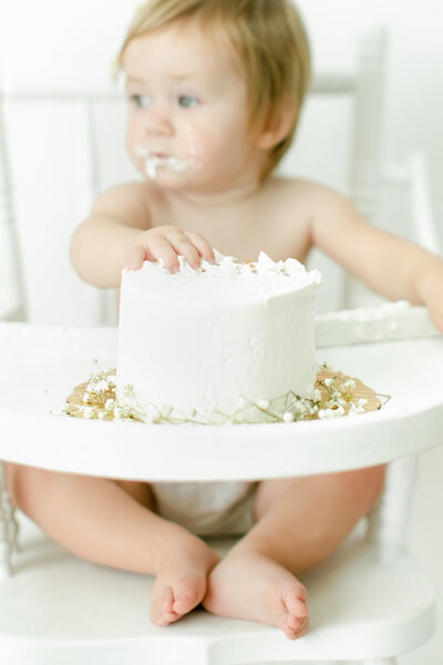 Photo of baby in high chair with hands in cake 