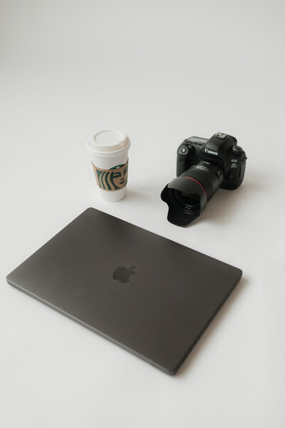 A laptop on the ground with a camera and coffee cup behind it 