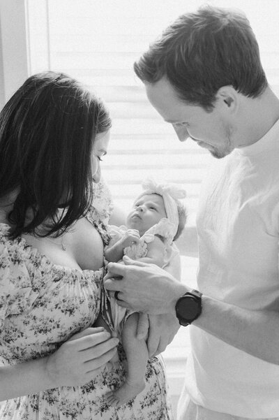 Parents admire their newborn baby near a sunlit window during an intimate in-home session captured by a Northern Virginia family photographer.