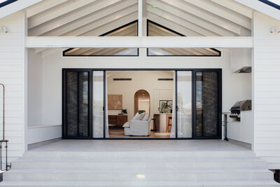 Modern house with open sliding doors, revealing a bright living room curated by a Newcastle interior designer, featuring a white couch and a grill on the side.