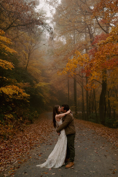 A bride and groom pose for elopement photos on a fall mountaintop.